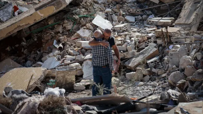 صورة تظهر رجلين يعانقان بعضهما وسط ركام مبنى مدمّر في لبنان
