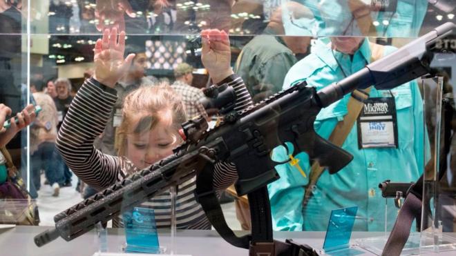 A girl looks at a gun on display
