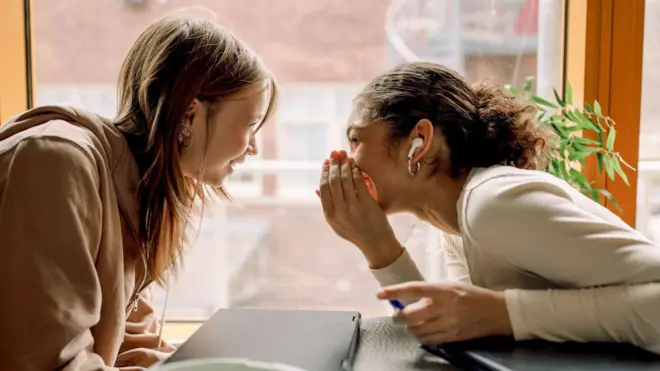 İki genç kadın karşılıklı dedikodu yapıyor ve gülüşüyor