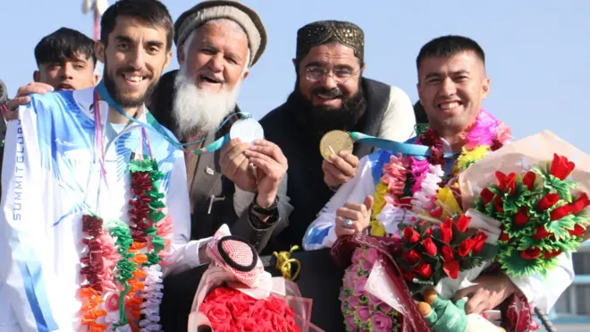 سمت راست ورزشکار افغان که گلهای رنگارنگ در دست دارد.و مدال طلای او در دست فرد کناری او که کرتی و کلاه سیاه دارد. در سمت چپ هم ورزشکار دیگر با پیران سفید که گل در گردن دارد و مدال نقره او در دست فردی کنارش دارای ریش سفید دراز و کلاه روشن بر سر دارد.