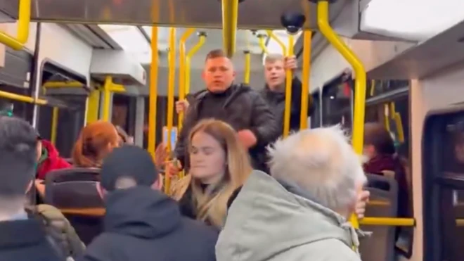 Зображення зсередини трамваю, на передньому плані чоловік і жінка, чоловік обернувся назад, за ним двоє чоловіків, які очевидно щось йому говорять, у трамваї багато інших пасажирів