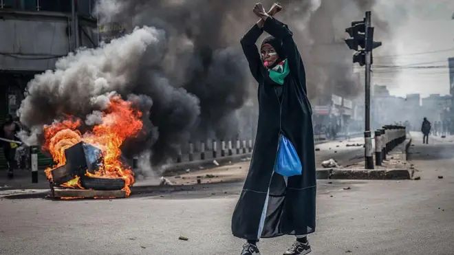  A protester wit her hands up in front of a burning barricade in downtown Nairobi on June 25, 2025 during a planned day of protest to mark di first anniversary of di storming of di parliament