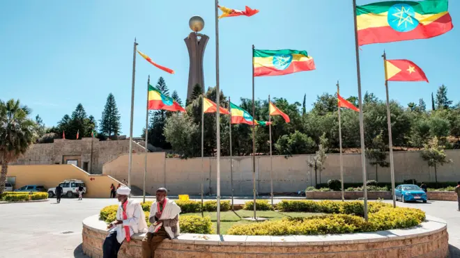 የኢትዮጵያ እና የትግራይ ክልል ባንዲራዎች የተሰቀሉበት ስፍራ ስር የተቀመጡ አዛውንቶች
