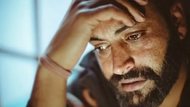 Bearded man holding his head in his hand and tearing up