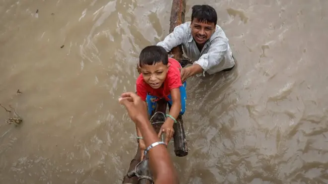 A man helps his son climb above a flooded street in Delhi