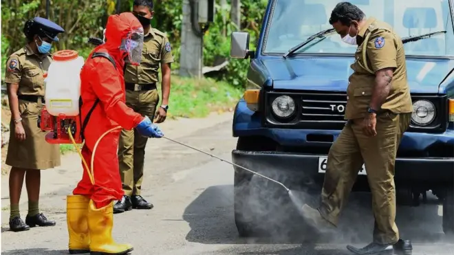 A municipal worker sprays disinfectant on a police officer's shoes in Atulugama on March 29, 2020, after the town that was sealed off by health authorities following fears that it could be a cluster for COVID-19 infection after two people tested positive for the virus. - Sri Lanka is currently under an indefinite curfew to prevent the spread of the virus which has already infected 115 people