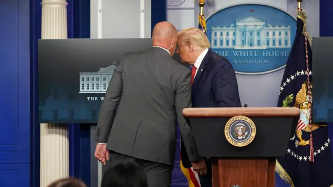 US President Donald Trump talks with a secret service agent before leaving a coronavirus briefing at the White House, August 10, 2020