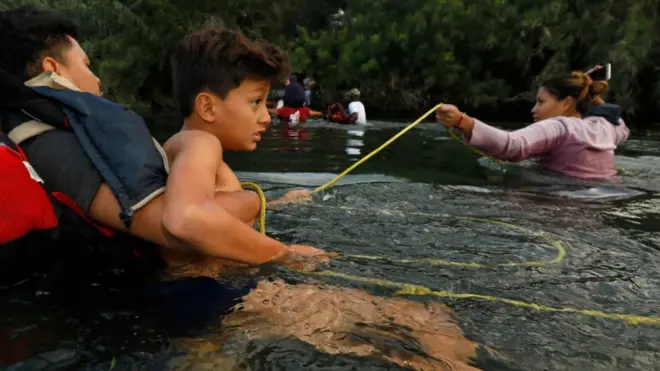 Muchos migrantes cruzan el río nadando sujetándose de una soga.