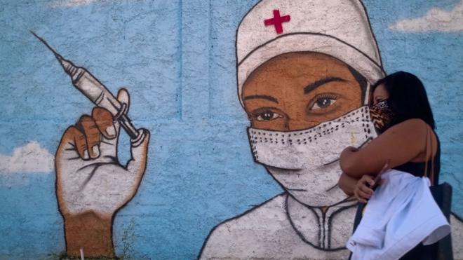 Mulher de máscara passa em frente a mural com grafite de vacinação no Rio de Janeiro, em 31 de julho de 2021