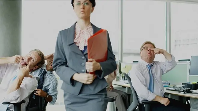 Dos empleados haciéndole morisquetas a una jefa a sus espaldas