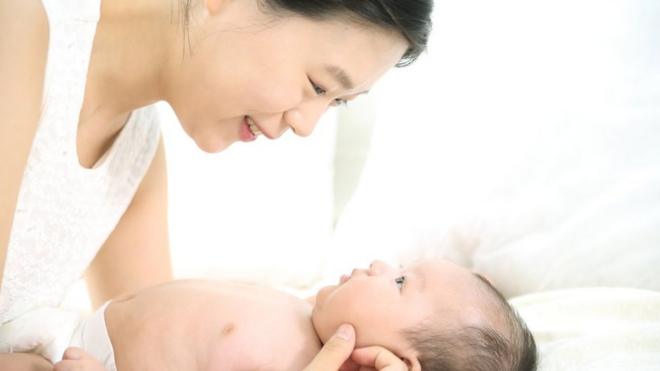 Mulher olha sorrindo para bebê deitado