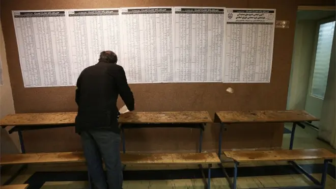 ناخب يملأ بطاقة التصويت وأمامه قوائم المرشحين في طهران.