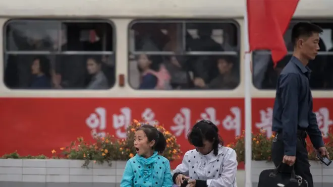 평양 기차역 밖에 시민들이 앉아 있다.