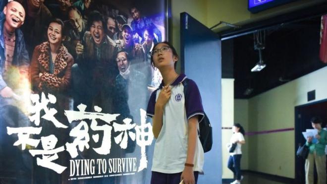 In this picture taken on July 12, 2018, a girl walks past a poster of the film 'Dying to Survive' at a cinema in Beijing