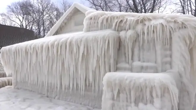 A house is seen completely encased in ice - but still recognisable as a shape - encased in icicles