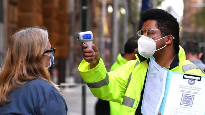 A health worker scans the temperature of someone waiting to enter a medical clinic in Sydney