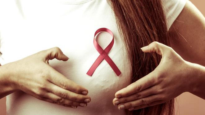 Jeune femme tenant un de ses seins avec le ruban représentant la lutte contre le cancer du sein.