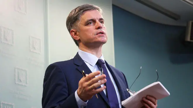 Вадим Пристайко в костюмі на тлі світло-блакитної стіни з логотипом Офісу президента