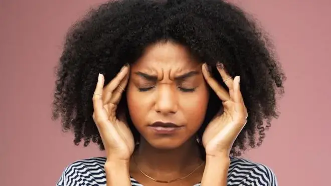 Umugore urwaye umutwe, arahumirije, ibiganza bye bifashe ku mutwe. Bigaragara ko arimo kubabara. 