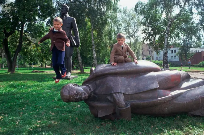 Yerde bir heykel, üzerinde iki çocuk oynuyor