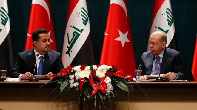 Irak Başbakanı Muhammed Şiya el-Sudani ve Cumhurbaşkanı Recep Tayyip Erdoğan birbirine bakıyor. Arkada Türkiye ve Irak bayrakları var