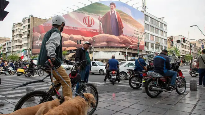Motorists pass under a banner featuring a portrait of Mojtaba Khamenei, Iran's new Supreme Leader, on a busy street in Tehran
