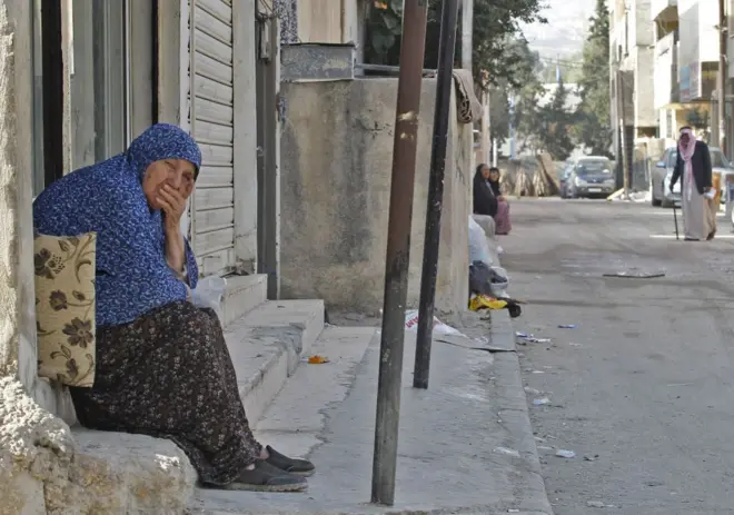 مسنة تجلس في زقاق داخل مخيم البقعة، الأردن.