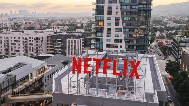 O telhado dos escritórios da Netflix em Los Angeles, com um grande letreiro vermelho NETFLIX em primeiro plano e a paisagem urbana ao fundo