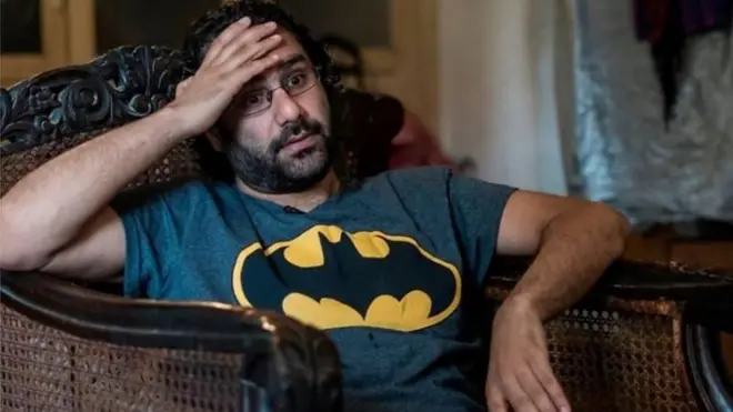 علاء عبالفتاح يرتدي تي شيرت عليه صورة وطواط، ويجلس على كرسي واضعا يده فوق رأسه