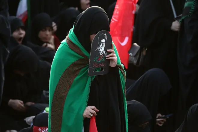 امرأة تغطي وجهها بصورة لعلي خامنئي خلال التشييع في قم