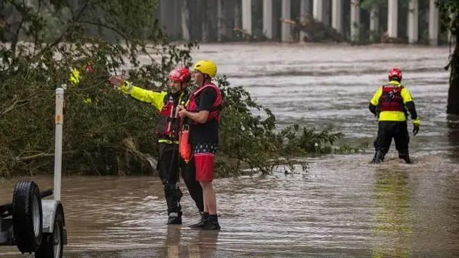 黄色と赤の救助服とヘルメットを着けた隊員たちが、氾濫した川の中に立ち、捜索活動にあたっている