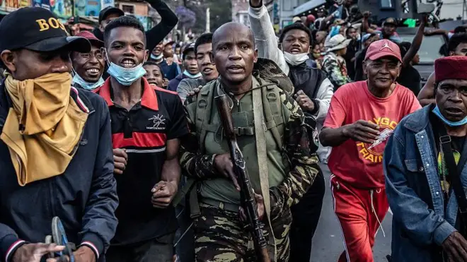 Военный с автоматом в руках идет посреди протестующих