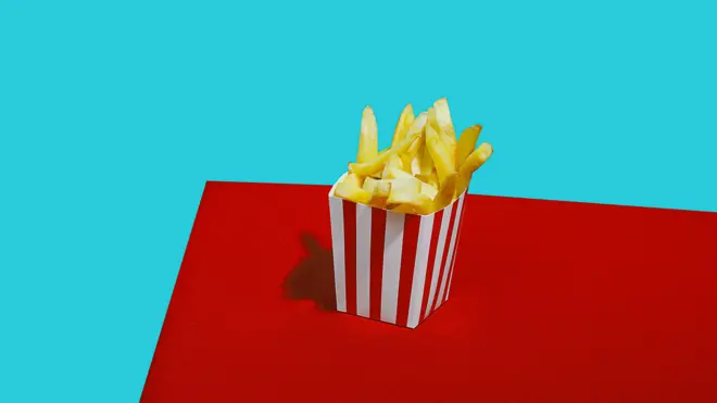 Mavi arka plan önünde, masa üzerinde karton bir kutuda patates kızartması.
