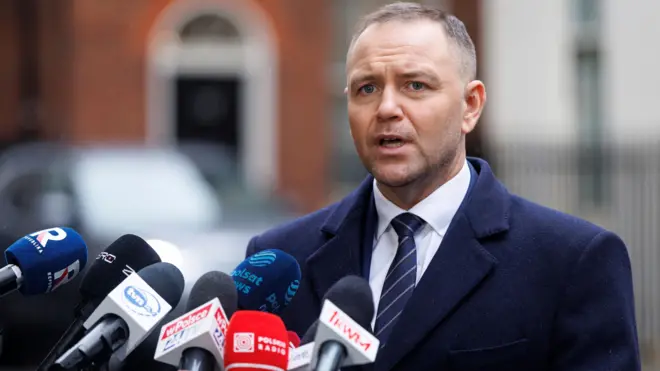 Polish President Karol Nawrocki, dressed in a blue suit with white shirt and blue tie, stands in front of a bunch of media microphones on Downing Street in central London.
