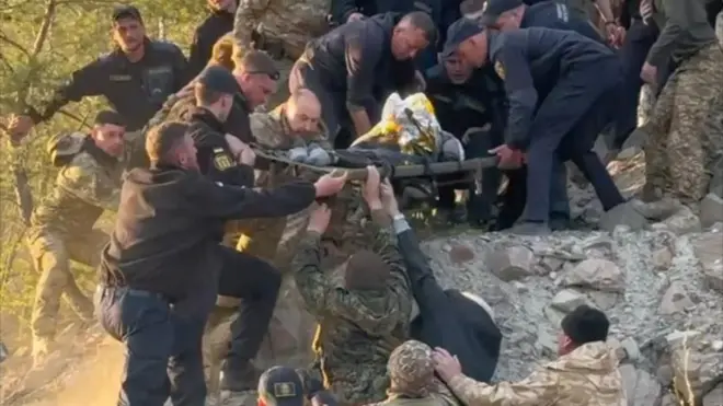 Фото в карʼєрі, багато чоловіків тримають ноші, інші знизу підтримують тих, хто зверху