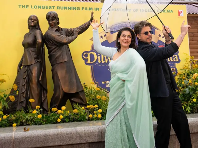 يظهر شاروخان وكاجول ديفغان وهما يلتقطان الصور خلال إزاحة الستار عن تمثال برونزي جديد يجسّدهما، وذلك في فعالية إطلاق تمثال رجوع العاشث المجنون ضمن مسار مشاهد في الساحة في ليستر سكوير، في 4 ديسمبر/كانون الأول 2025 في لندن، إنجلترا.