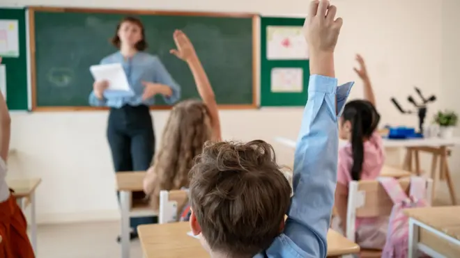 Students raising their hands in a classroom.