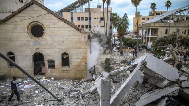 يمرّ الناس أمام مبانٍ متضررة وأنقاض مستشفى المعمدانيين في مدينة غزة