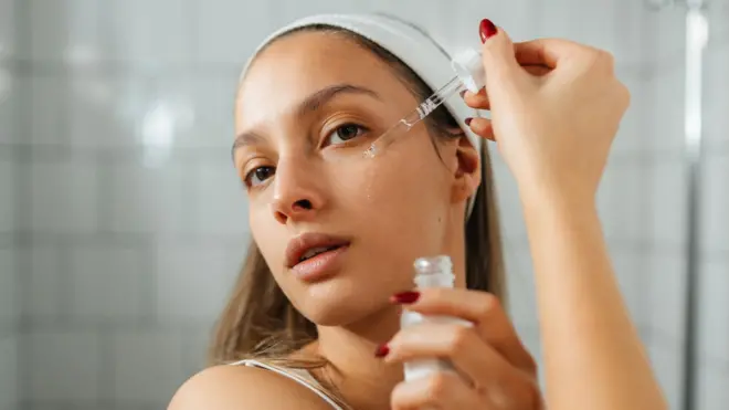 Młoda kobieta stoi w łazience i nakłada na twarz serum