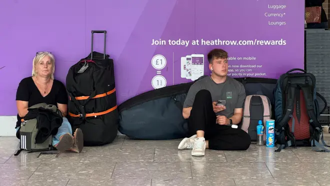 People sit on the floor in Heathrow's Terminal 4 beside their bags.