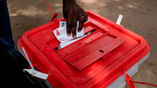 Hand of man wey wan drop vote inside ballot box