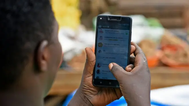 Une femme en train de parcourir son compte WhatsApp sur son téléphone à Kampala.