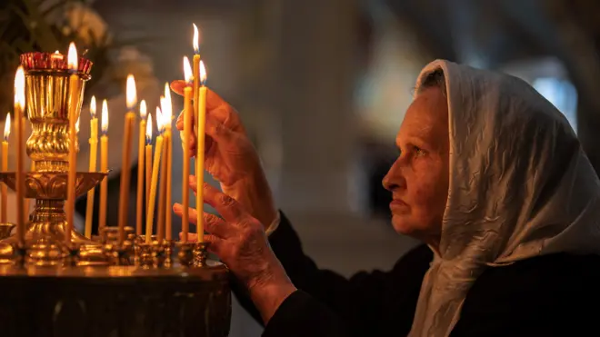 Украинская женщина в платке на голове зажигает свечи в храме