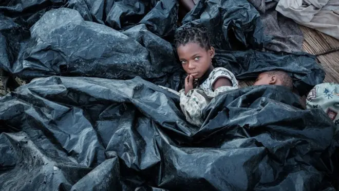 Enia Joaquin Luis, 11, aamka kando ya dada yake wa miaka sita, wakiwa wamejifunika mfuko wa plastiki kujikinga na mvua ,katika makazi ya muda ya Buzi. Hii ni baada ya kimbunga Idai kupiga pwani ya Msumbiji mwezi Machi 14 na kusababisha maafa na uharibifu mkubwa. Umoja wa Mataifa ulisema watu milioni 1.7 waliishi kwenye njia ya kimbunga hicho huku watu wengine 920,000 wakiathiriwa nchini Malawi na maelfu ya wengine nchini Zimbabwe.