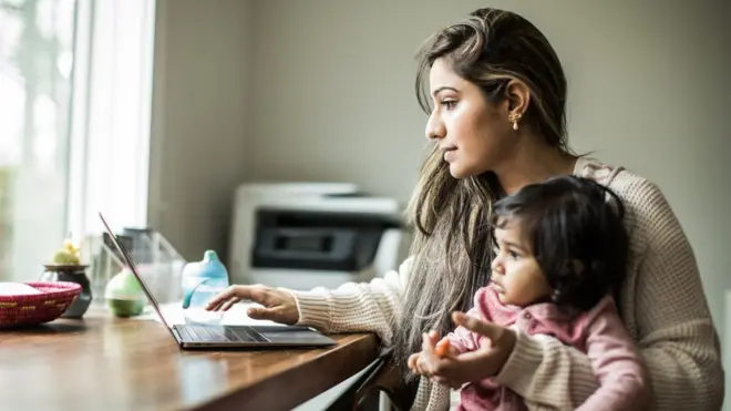 Mujer con una niña en brazos trabajando.