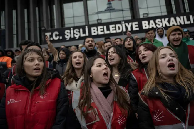 Şişli Belediyesi binası önünde kalabalık, önde bir polis, arkada Türk bayrağı ve Atatürk'ün resmi