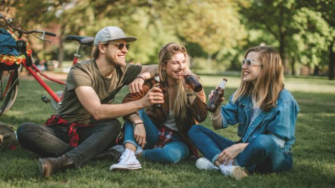 Grupo de amigos en un parque tomando cerveza con cervezas detrás.