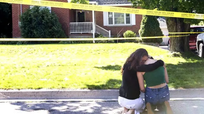 Two women console each other outside the house where the shooting took place