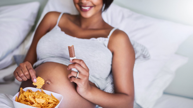 Femme noire enceinte mangeant du chocolat et des chips