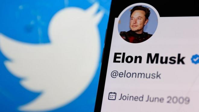 Elon Musk account on Twitter displayed on a phone screen and Twitter logo displayed on a laptop screen